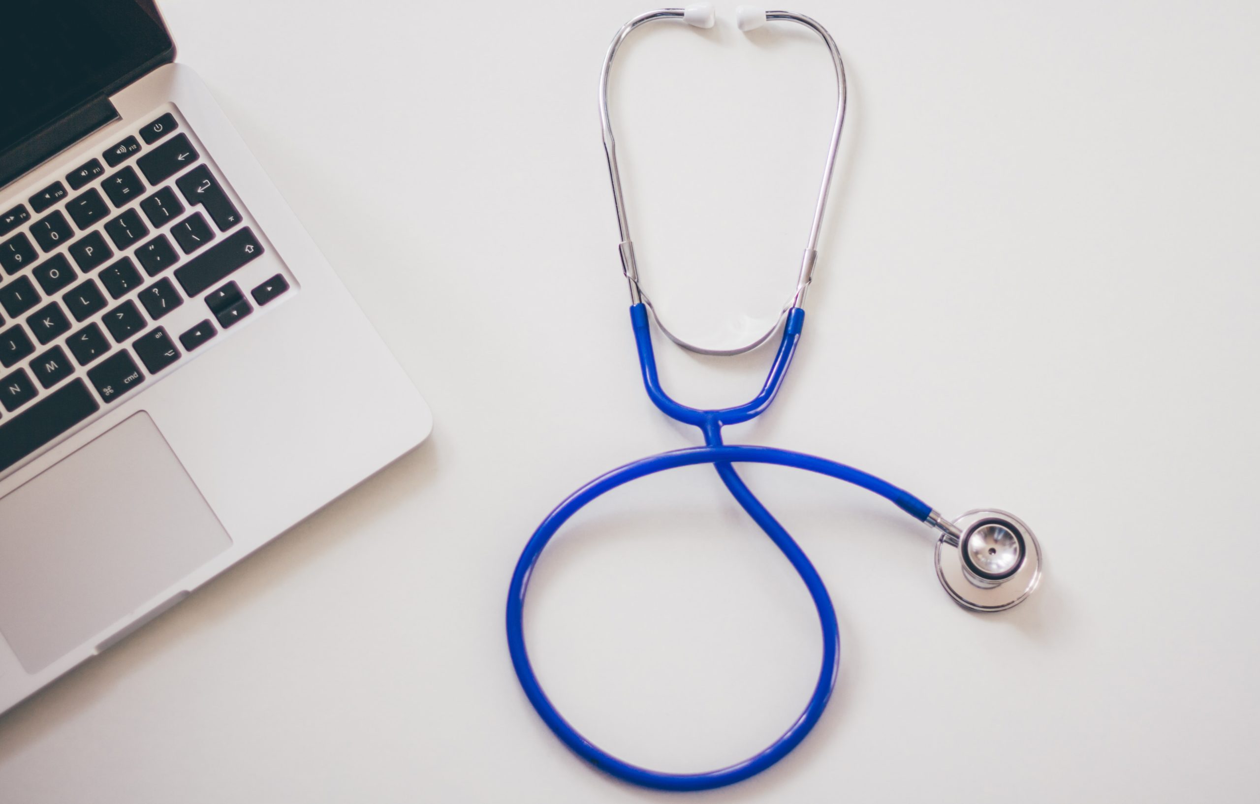 A stethoscope with a blue tube is coiled neatly next to an open laptop on a white surface, serving as a reminder to watch for hidden injuries that can arise after a car accident.