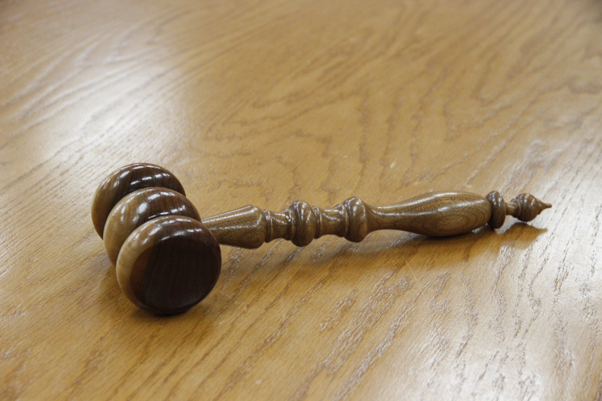 A wooden gavel with a detailed handle rests on a smooth wooden surface.