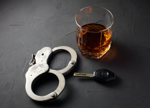 A glass of whiskey, a car key, and a pair of handcuffs sit ominously on a dark textured surface, painting a stark reminder of the consequences of DWI in Texas.
