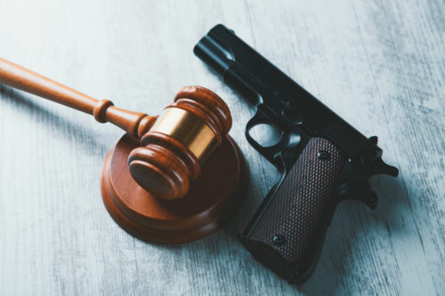 A wooden gavel and block beside a black handgun on a light wooden surface, symbolizing the intersection of Texas gun crime laws and firearms.