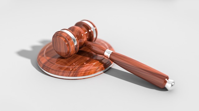 A wooden judge's gavel rests on a matching sound block against a plain, light background. The gavel and block are polished with metallic accents, symbolizing law and justice.