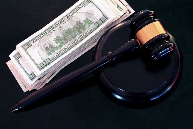 A judge’s gavel and sound block sit beside a stack of U.S. hundred-dollar bills on a dark surface, symbolizing the connection between bail, money, and the legal system.