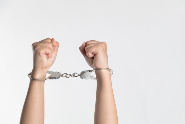 Two hands raised with clenched fists, both wrists secured in metal handcuffs—symbolizing the constraints of probation—against a plain white background.