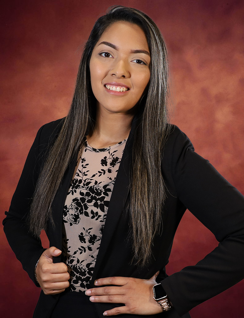 Crysthal Garcia, a woman with long brown hair, poses confidently in a black blazer over a patterned blouse. Her slight smile complements the warm, reddish-brown background.