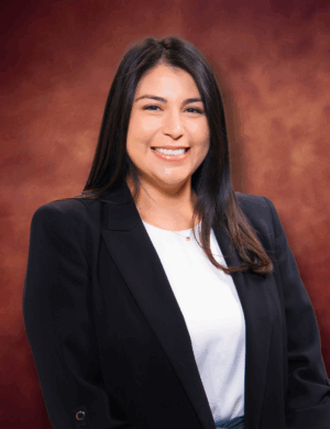 Chloe Martinez, a woman with long dark hair, is smiling while wearing a black blazer and white blouse. The background features a warm, brown gradient.