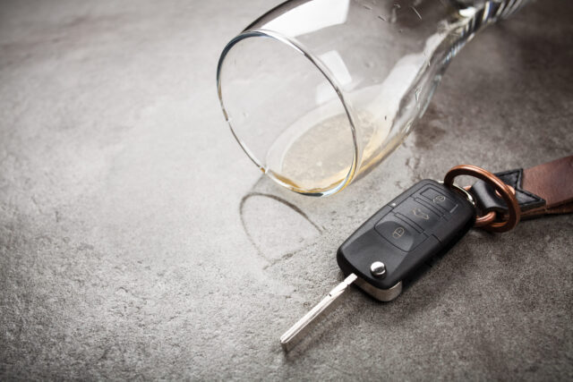 An overturned glass with a hint of liquid rests beside a car key fob on a gray surface, subtly suggesting the serious issue of drinking and driving in Texas. Understanding DWI defenses can be crucial in navigating the consequences.