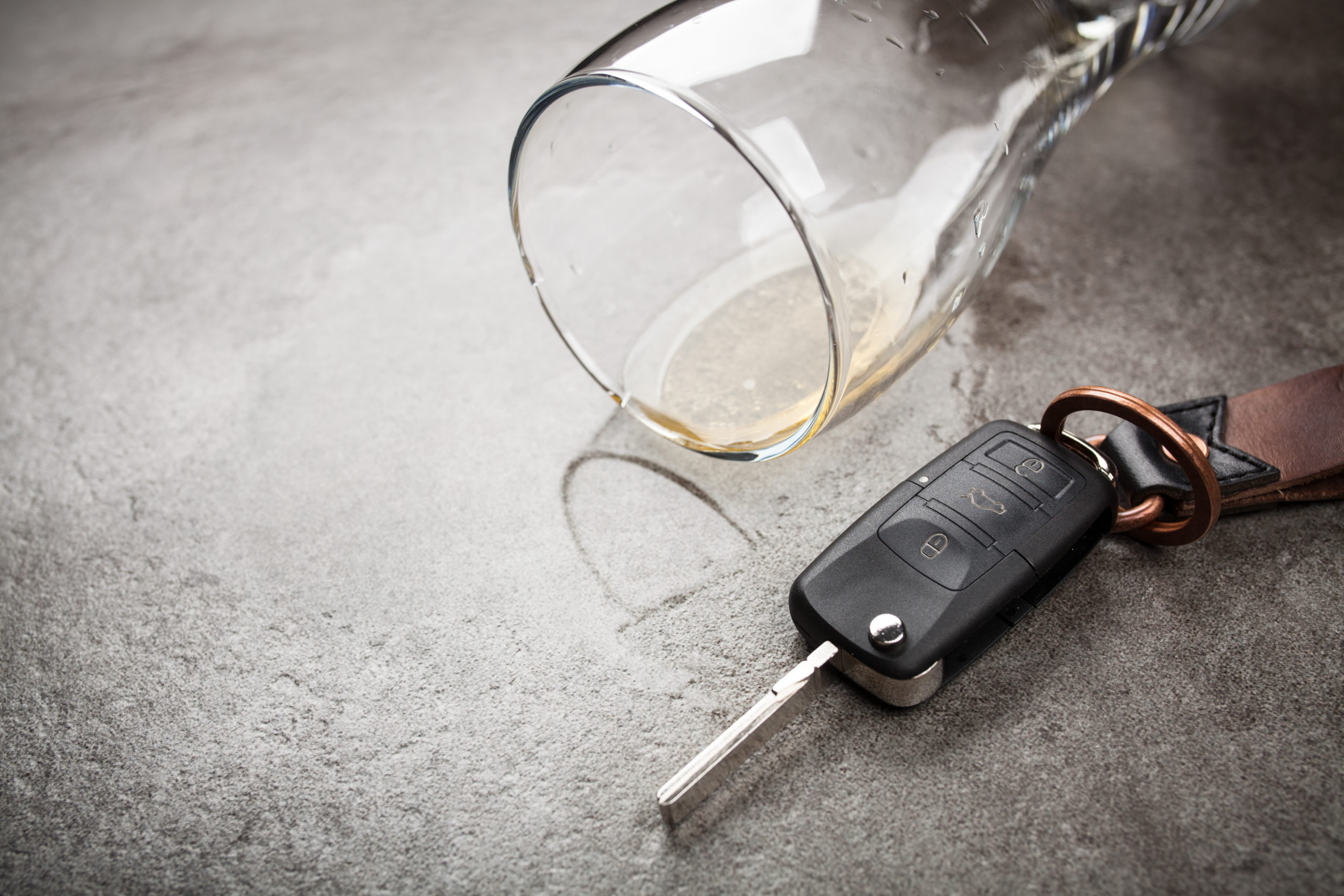 An overturned glass with a hint of liquid rests beside a car key fob on a gray surface, subtly suggesting the serious issue of drinking and driving in Texas. Understanding DWI defenses can be crucial in navigating the consequences.