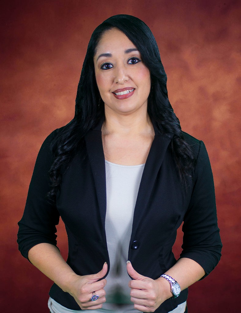 Gabby Martinez, a woman with long dark hair, smiles at the camera. She is wearing a black blazer over a light-colored top, her hands resting gracefully on her jacket. The background envelops her in a warm, gradient shade of brown.