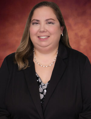 Christina Gardner, a woman with long brown hair, smiles at the camera. She is wearing a black blazer, a patterned blouse, and a pearl necklace. The background is a warm, reddish-brown gradient.