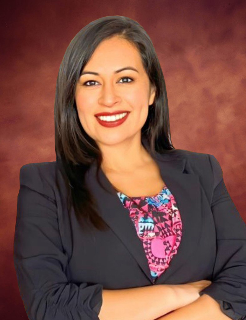 Jessica Ramos, a woman with long dark hair, smiles confidently while wearing a black blazer and a colorful patterned blouse. She stands poised against a warm-toned background.