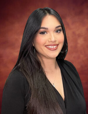 Stephanie Ortiz, with her long dark hair and radiant smile, stands out in a black top against a warm, textured background.