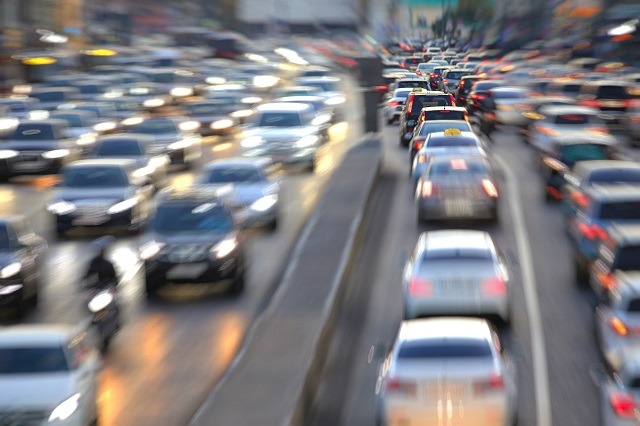 Blurred image of a busy urban street with heavy traffic, where cars are lined up in both directions. Headlights and taillights create a dynamic blend of colors, highlighting the deadly effects of congestion and the importance of traffic safety during rush hour.