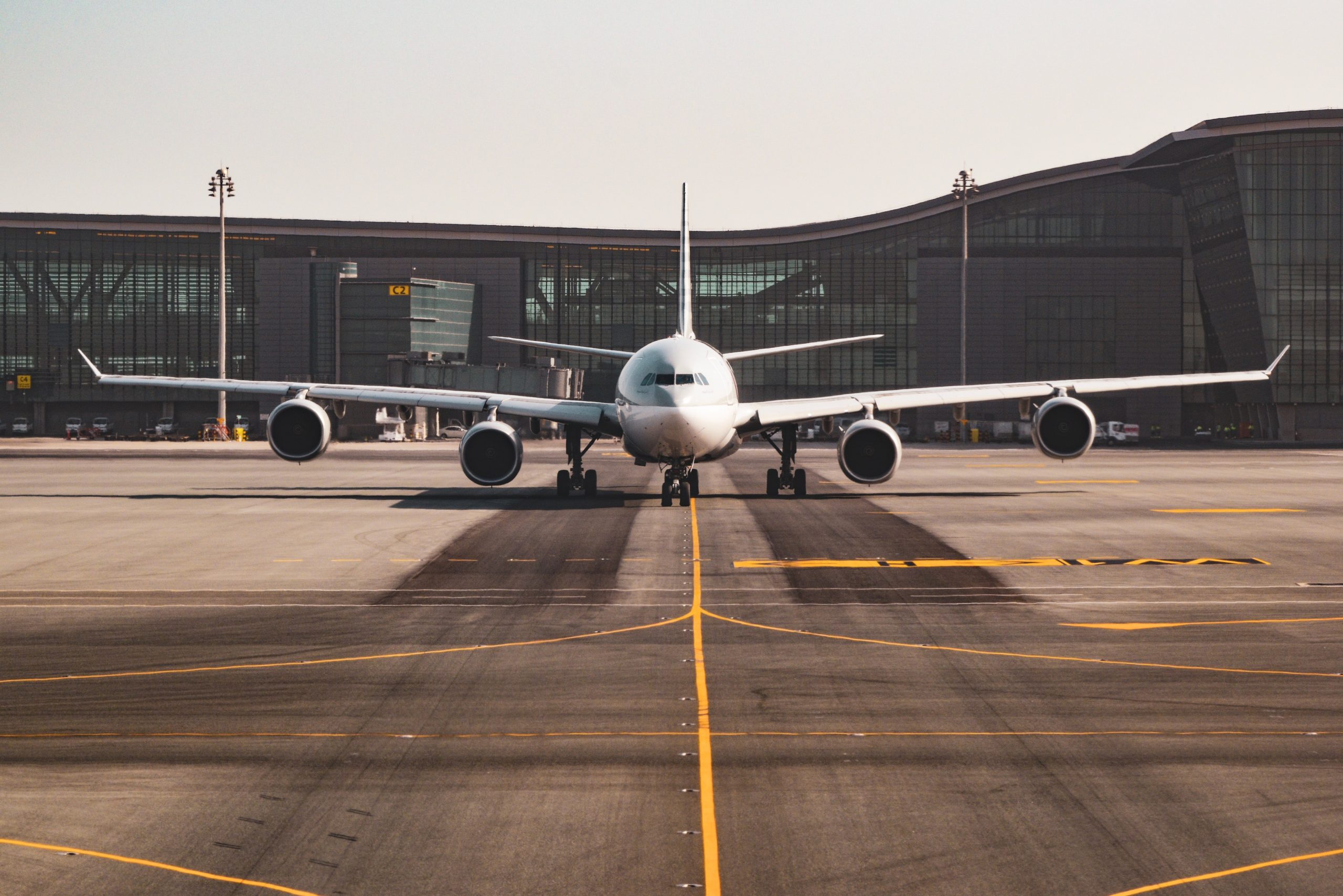 A large commercial airplane is stationary on a runway in front of a modern Texas airport terminal. The aircraft is viewed from the front, showing its wide wingspan and multiple engines under a clear sky—a scene where vigilance ensures airport accidents are kept at bay.