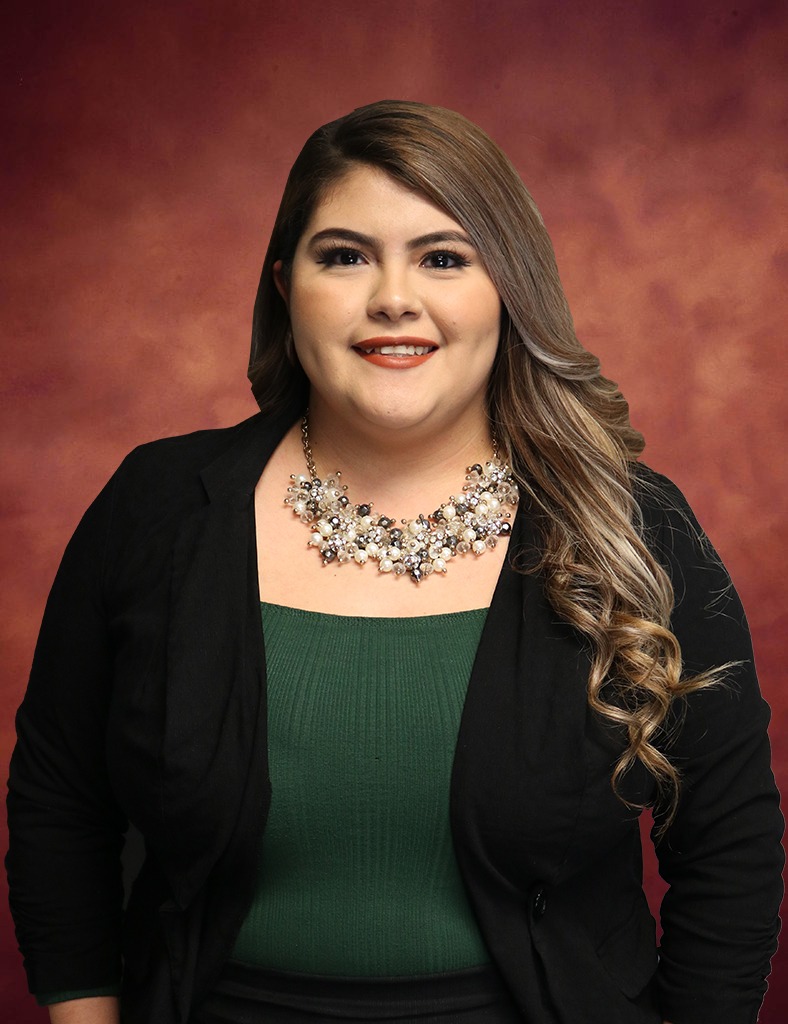 Cristal Galloso, a woman with long wavy hair, smiles at the camera. She is wearing a black blazer, green top, and a statement necklace. The background is a warm, reddish-brown gradient.