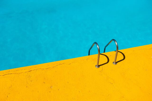 A bright yellow pool deck in Texas, featuring a sturdy metal ladder, leads into clear turquoise water. The vibrant colors create a striking contrast, evoking a sense of summer and leisure. Remember to always prioritize safety to avoid pool accidents while enjoying this serene setting.
