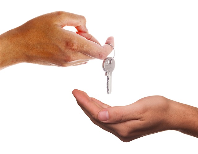 A close-up of two hands against a white background. One hand is holding and handing over a silver key to the other open, cupped hand, symbolizing the transfer or giving of the key—a poignant reminder of trust in real estate transactions amidst rising mortgage fraud cases in Texas.