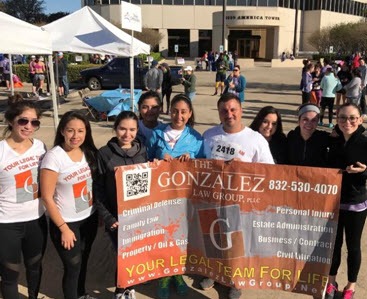 A group of people, some in matching shirts, pose outdoors holding a large banner for 
