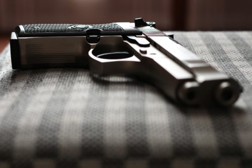 A licensed handgun rests on a textured, checkered surface. The metallic body contrasts with the dark grip pattern and is positioned horizontally, showing the barrel and trigger. For Texans who choose to carry handguns, attention to detail like this matters. The background remains softly blurred.