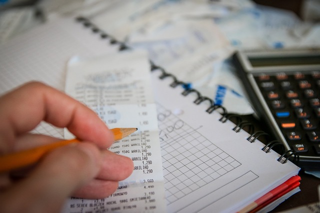 A hand grips a pencil, reviewing a lengthy receipt alongside a calculator on a graph-lined notebook. In the blurred background, documents hint at budgeting or accounting—perhaps assessing penalties for potential tax evasion in Texas.