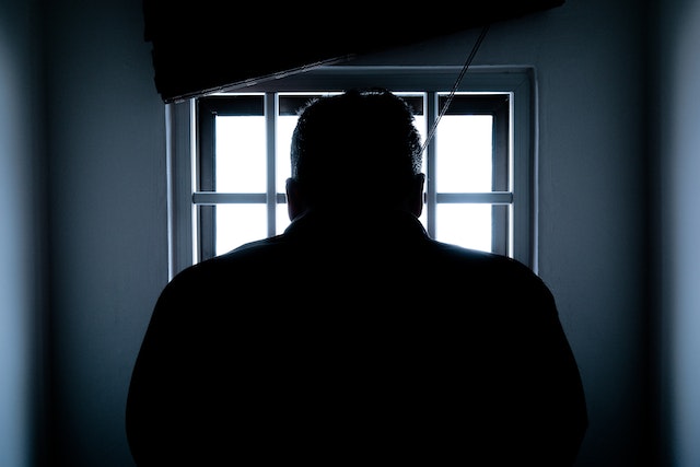 A person silhouetted against a bright window in Texas, facing away, with light streaming through bars. The image conveys a sense of solitude and introspection, perhaps reflecting on self-defense laws or other legal information.