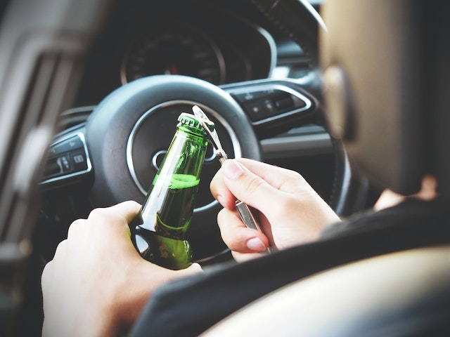 person opening beer bottle while sitting in car driver's seat