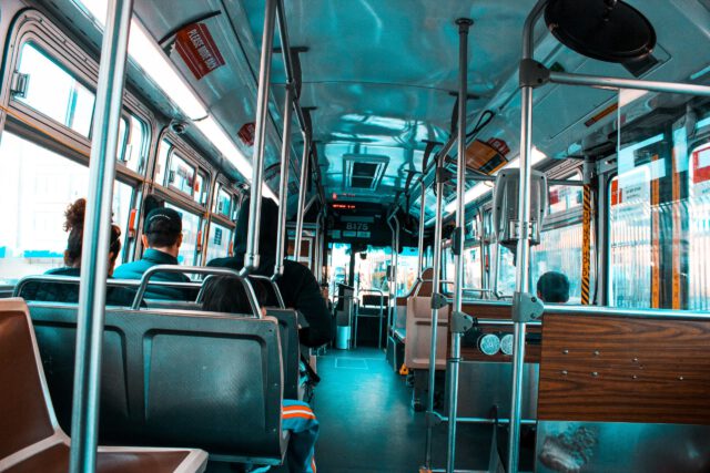 Interior view of a city bus with passengers seated, capturing the everyday public transport atmosphere in Texas. The photo shows the aisle, seating, and overhead handles, while a few windows display a cityscape in the background, reminding us of bustling city life amidst concerns about bus accidents.