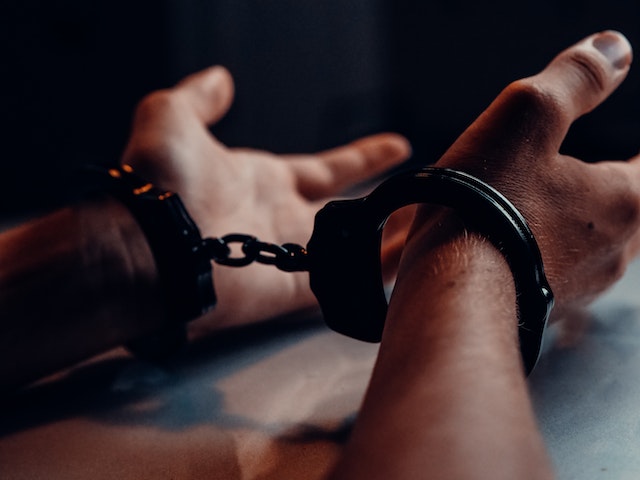 Close-up of a person’s hands in handcuffs resting on a surface, highlighting the severity of their situation. Dim lighting creates a dramatic and tense atmosphere, focusing on the wrists and cuffs. The scene captures the gravity often associated with a Texas felony charge.
