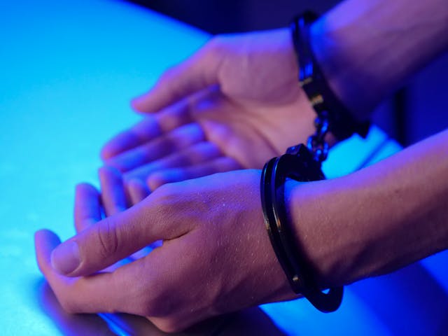 Hands in handcuffs beneath a blue light, with fingers slightly spread apart, resting on a surface—a somber reminder of the consequences tied to domestic violence charges.
