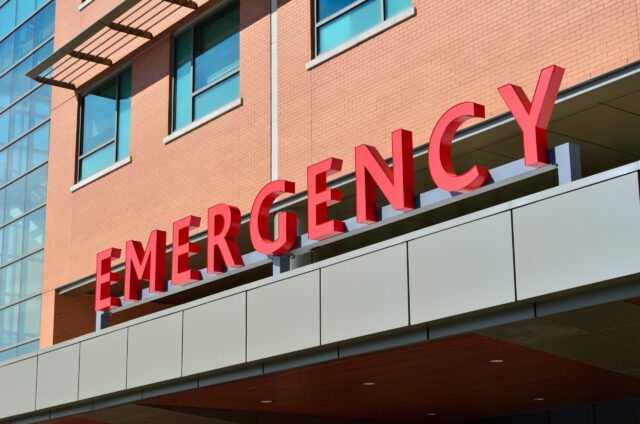 A large red emergency sign adorns the exterior of a building, hinting at a hospital or medical facility entrance. With its brick facade and glass windows above, one might question if product liability lawsuits are as common here in Texas as they are elsewhere.