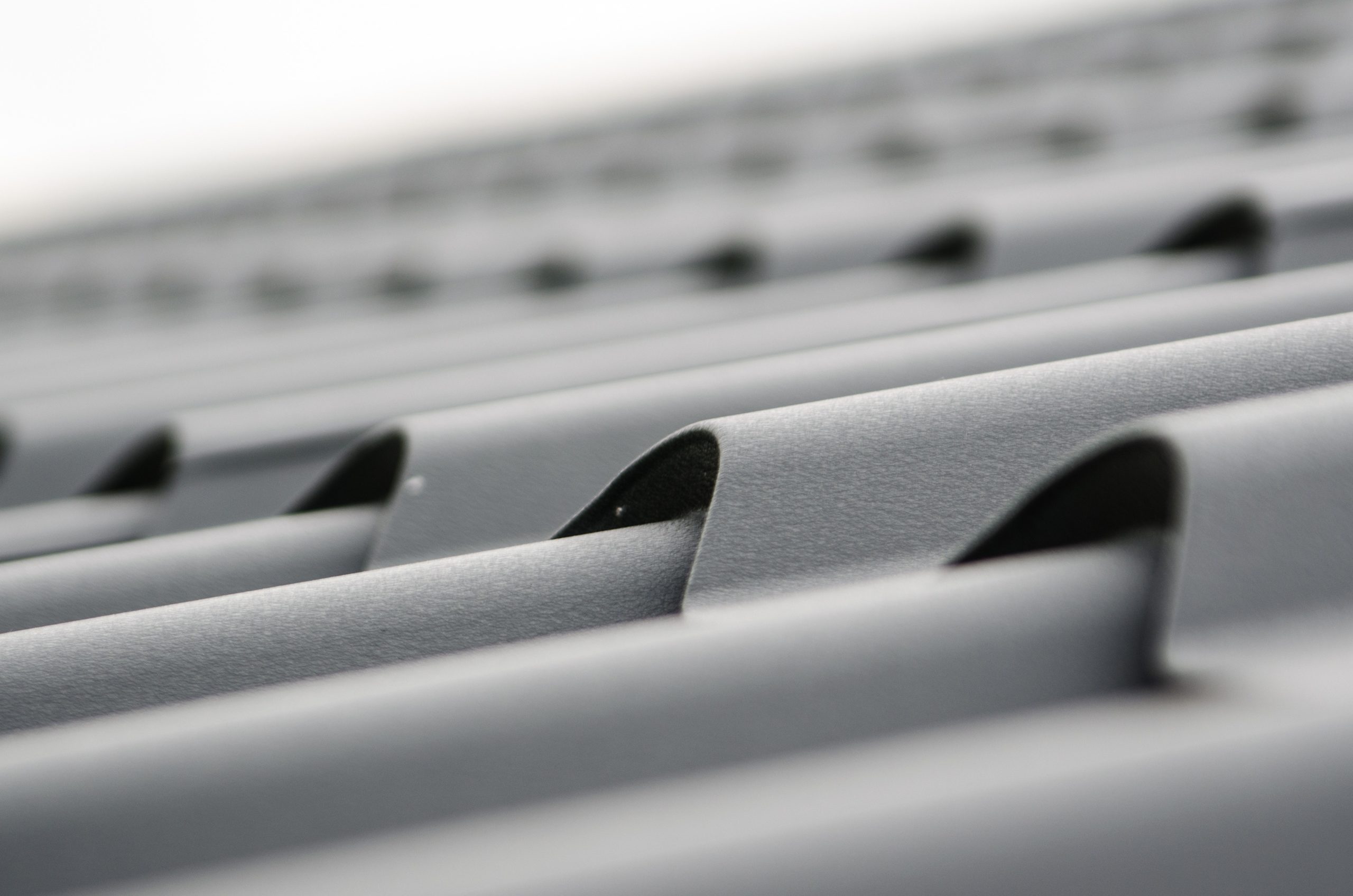 Close-up of a grey, corrugated metal roof showing the parallel ridges and grooves extending into the distance, creating a pattern of lines and shadows. The focus is on the texture and structure, highlighting its resilience against unexpected damages.