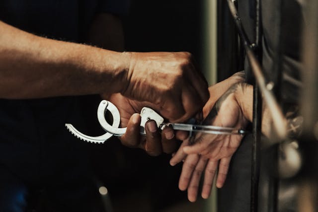 A person's hands being handcuffed by another individual, possibly indicating a DWI arrest. The scene appears to be indoors with a close-up focus on the hands and handcuffs, conveying a sense of detainment.