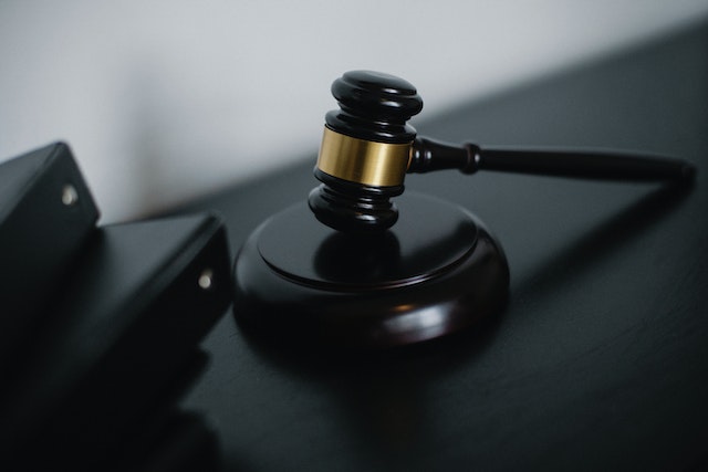 A close-up of a wooden judge's gavel resting on a sounding block, placed on a dark table evokes the seriousness of Texas trafficking charges. Nearby, blurred black folders hint at legal proceedings tied to fentanyl trafficking, underscoring the weight of justice in the courtroom setting.