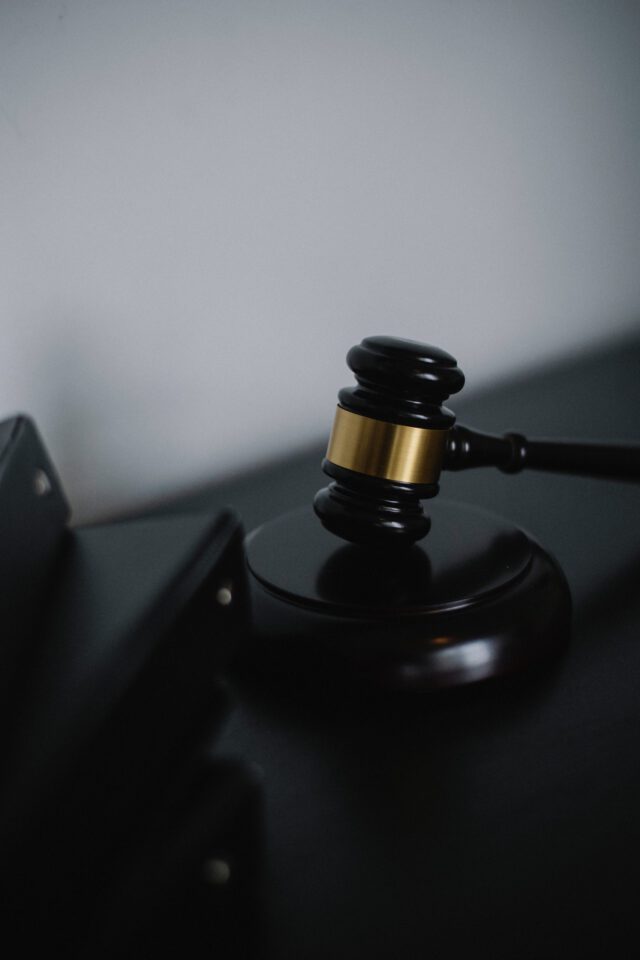 A close-up of a judge's wooden gavel, embellished with a metallic gold accent, resting on a sound block. In the blurred background reminiscent of a Texas firm's chambers, dark surfaces enhance the formality and seriousness, as if preparing for an initial consultation.