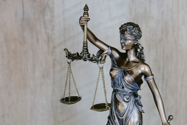 A bronze statue of Lady Justice, blindfolded and holding a set of scales in her left hand, symbolizes fairness and equality under the law—a reminder that justice prevails even when seeking Texas DWI expungement. The background is softly blurred wood texture.
