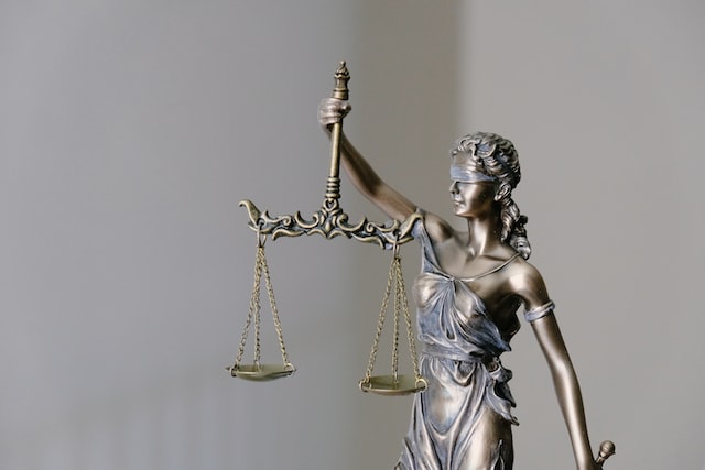 A bronze statue of Lady Justice balances scales in her right hand, blindfolded to symbolize impartiality—an enduring symbol for those facing a DWI charge. The background remains a neutral, blurred gray, emphasizing the statue's solemn presence.