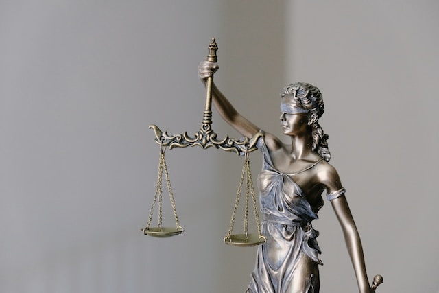 A bronze statue of Lady Justice stands firm, blindfolded to symbolize impartiality, clutching balanced scales and a sword representing Legal Rights. The soft, neutral background enhances the solemnity of her figure as an emblem of justice.