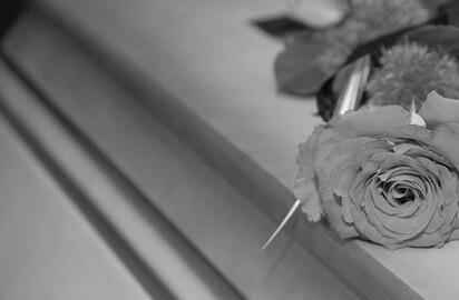 A black and white image of a rose delicately resting on a closed casket captures the somber mood of mourning and remembrance, evoking thoughts of una muerte injusta por negligencia.