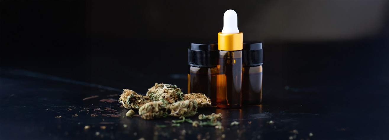 Three small amber bottles, two with black caps and one with a white dropper cap, are placed on a dark surface. Next to them are dried cannabis buds. The background is a subtle gradient from dark to light.