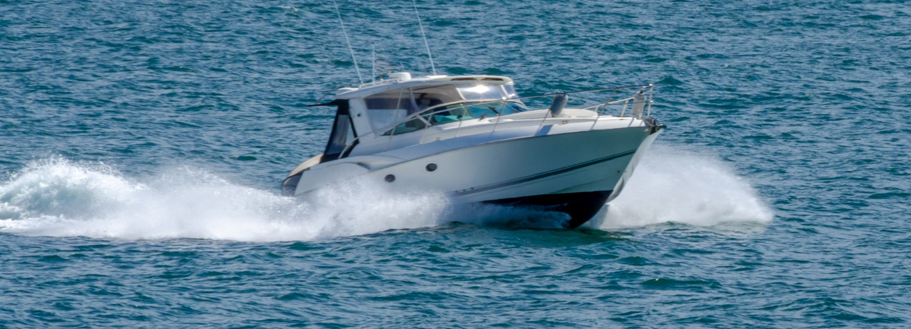 A white motorboat speeds across clear blue water, creating white foam and waves in its wake on a sunny day.