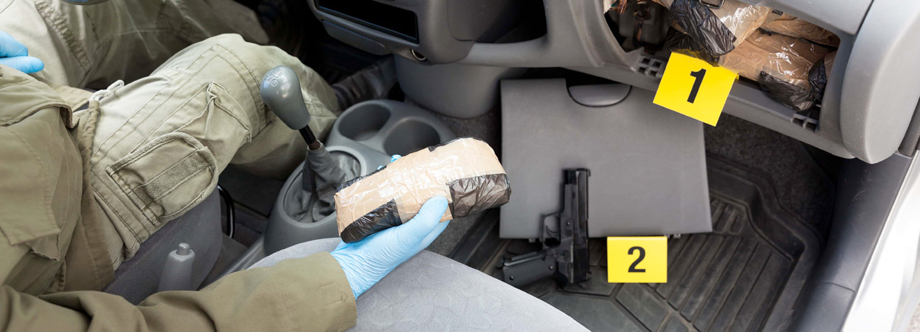 A person wearing gloves is holding a package wrapped in brown tape inside a car. Another package is in the glove compartment labeled 