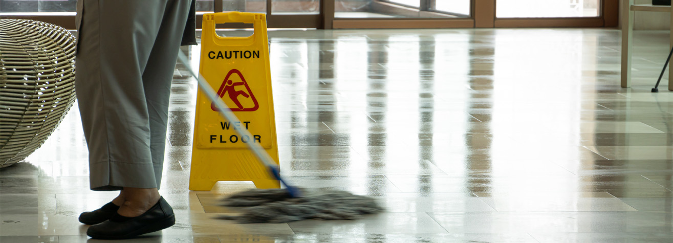 A person mops a shiny floor next to a yellow caution sign that reads 