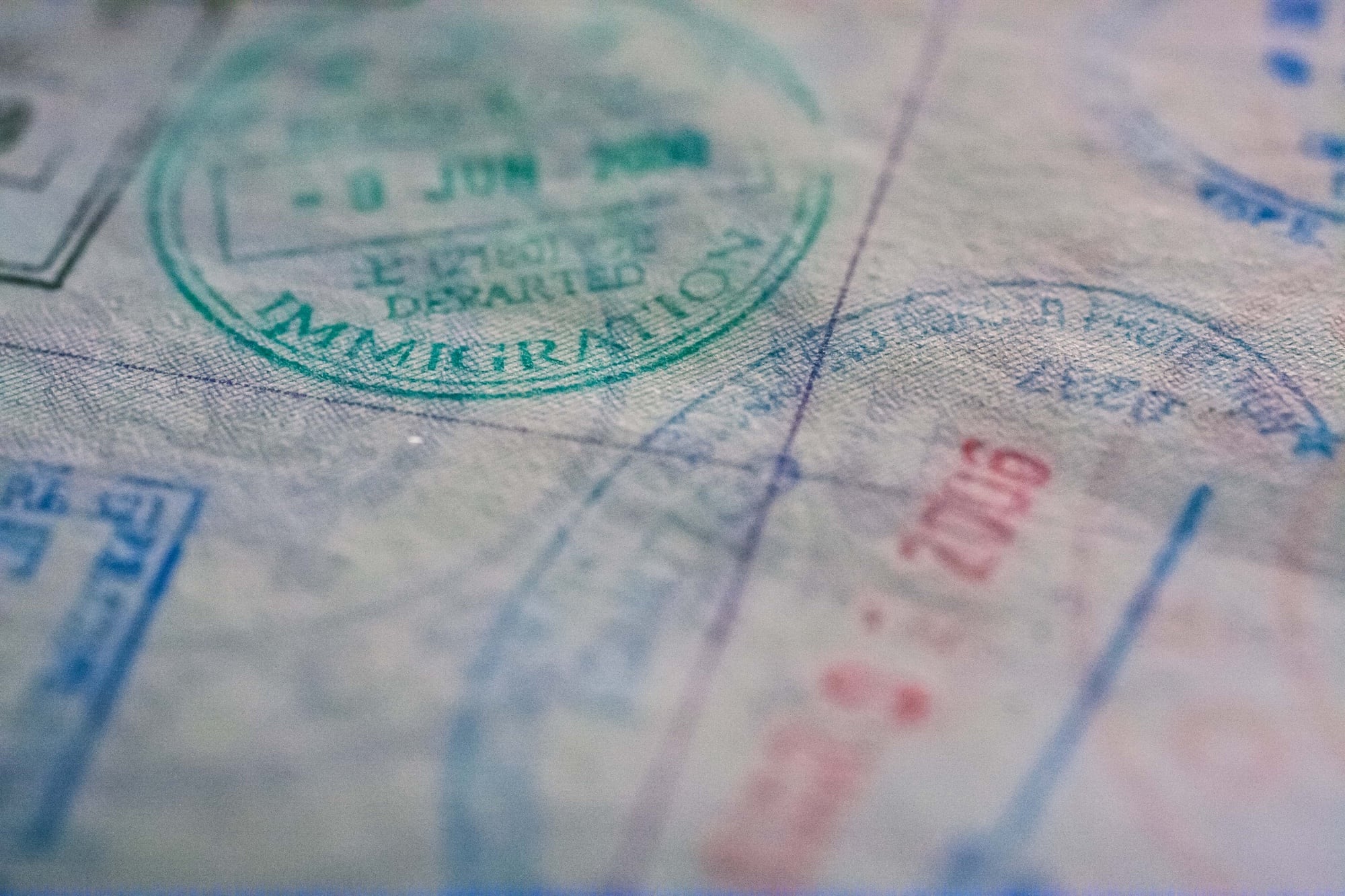 Close-up of a passport page featuring multiple immigration and travel stamps in various colors including green and red. The image is slightly blurred, giving a sense of movement and travel history.