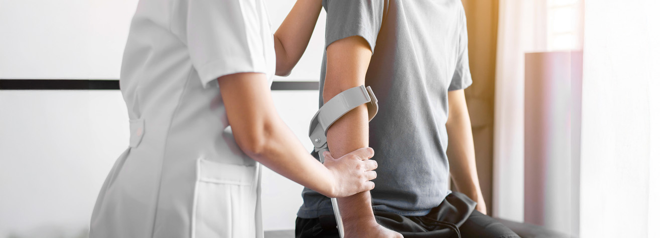 In a medical office, a healthcare professional assists an individual in a gray short-sleeve shirt on the examination table, gently supporting their elbow. This attentive care often aligns with services provided by professionals like a Baytown personal injury lawyer.
