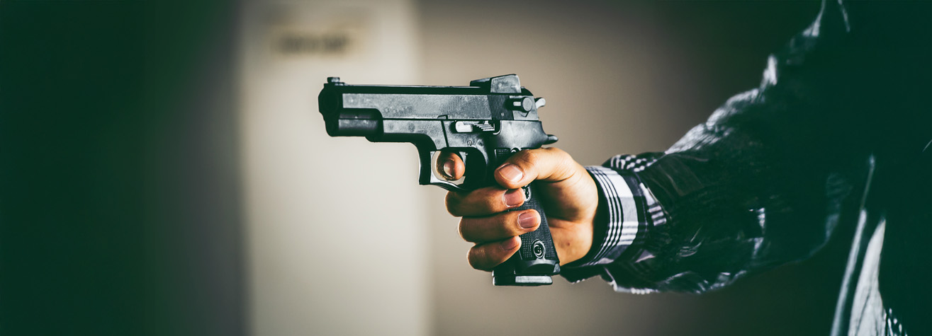 A person in a suit aims a black handgun, holding it with one hand. The background is blurred, focusing attention on the firearm.