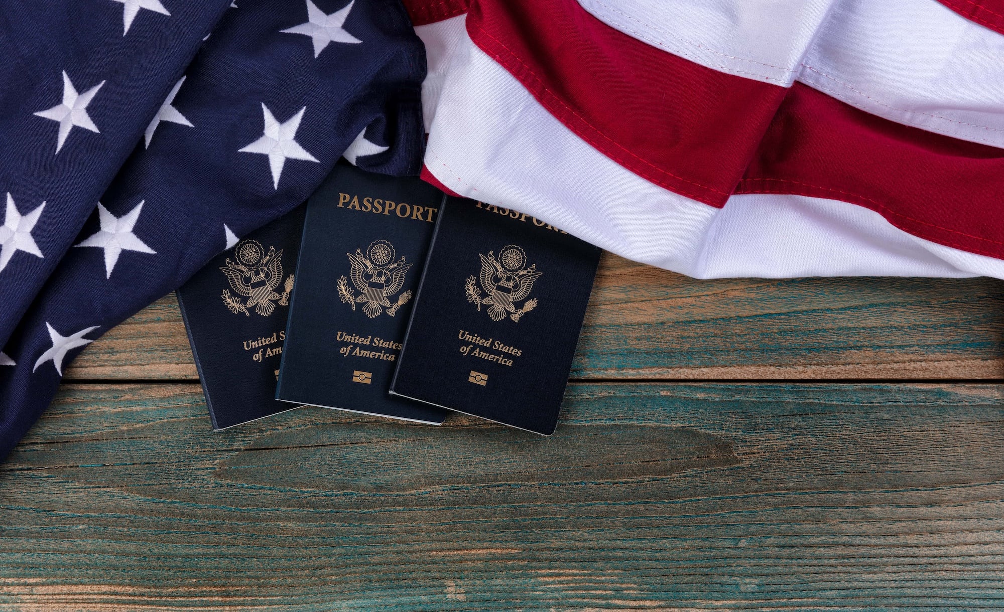 Three U.S. passports are displayed on a wooden surface, partially covered by the American flag with visible stars and stripes.