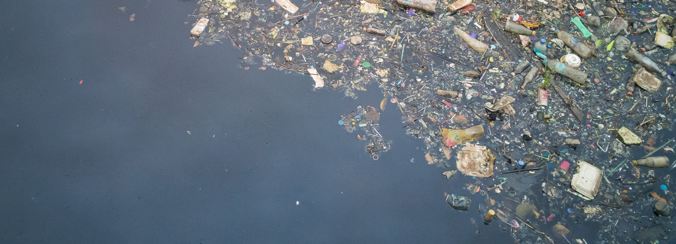 A polluted body of water with various debris floating on the surface, including plastic bottles, containers, and other waste, creating a stark contrast with the water's dark, murky appearance.