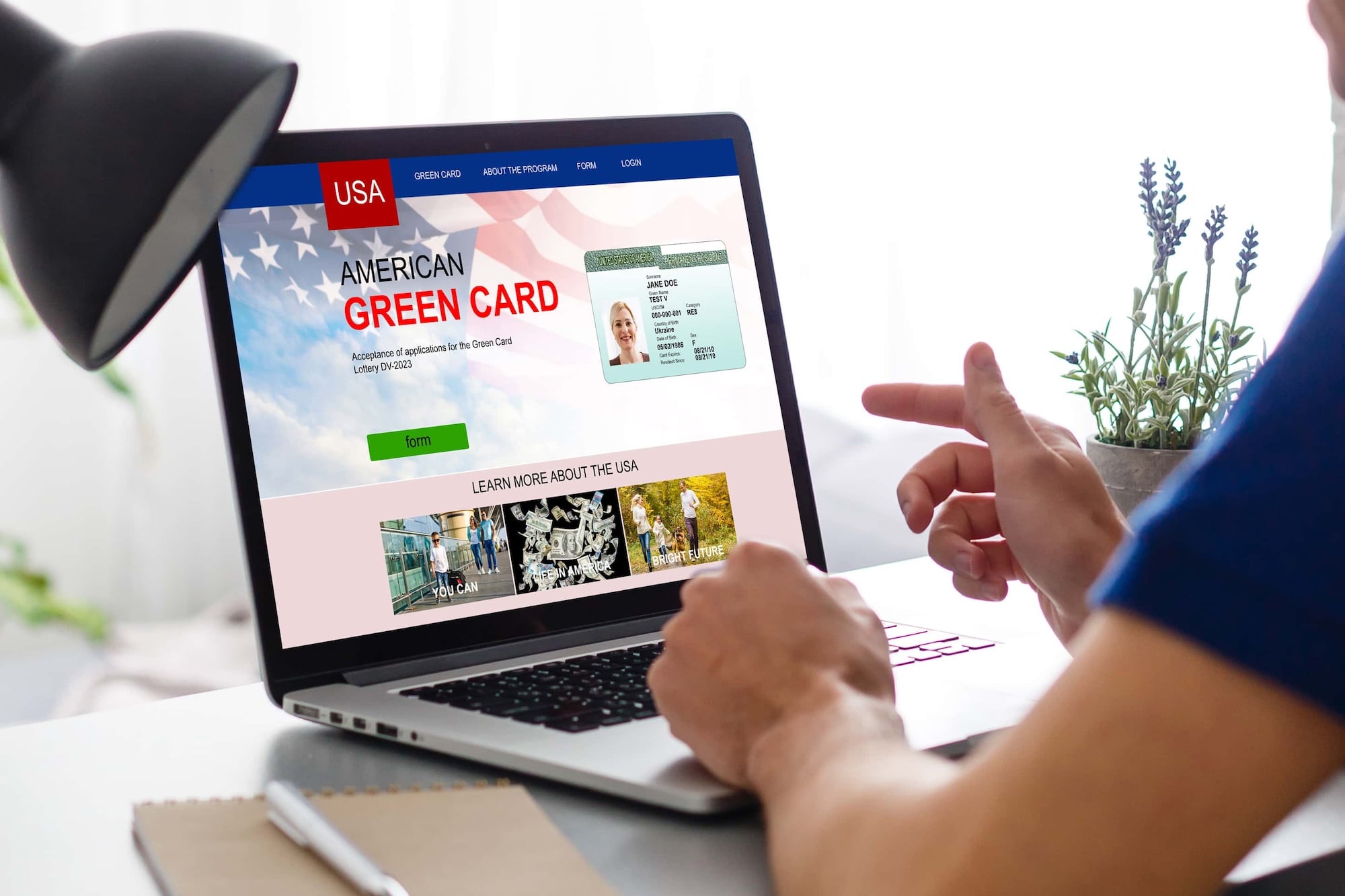 Person sitting at a desk using a laptop displaying a website for the American Green Card application. The screen shows application details, a sample Green Card image, and a 