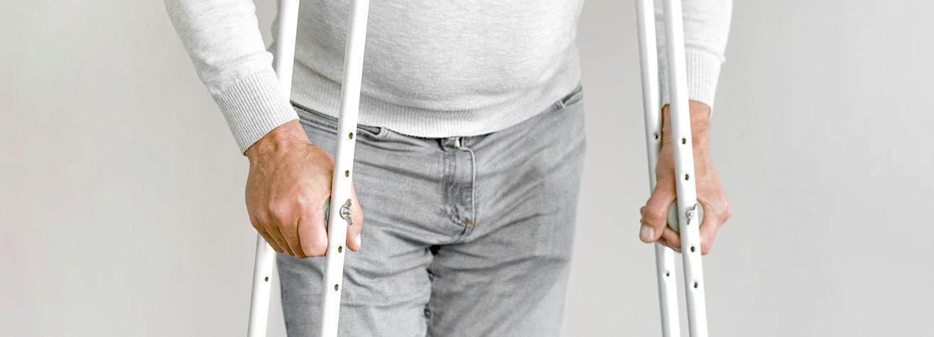 A person in a light gray sweater and jeans is seen using crutches, their hands gripping them firmly—a common sight in Galena Park after a personal injury. The background is plain white, emphasizing the focus on recovery.