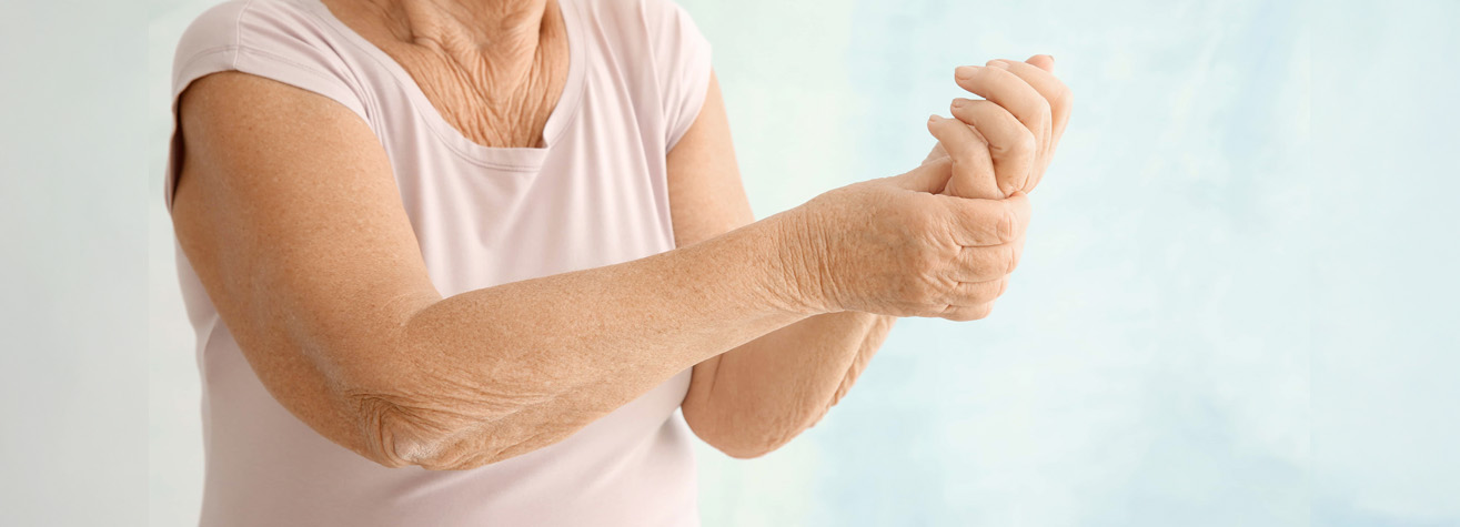 An elderly person in a light pink shirt holds their wrist with the other hand, possibly due to discomfort, against a light blue background—an image capturing the essence of personal injury struggles in bustling Houston.