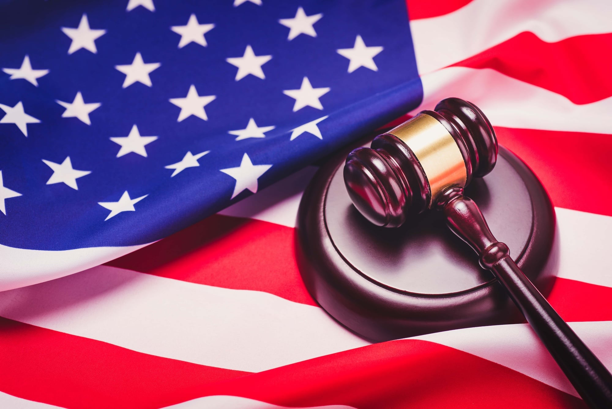 A wooden gavel rests on its sound block atop an American flag. The flag's stars and stripes are visible, symbolizing justice and patriotism.